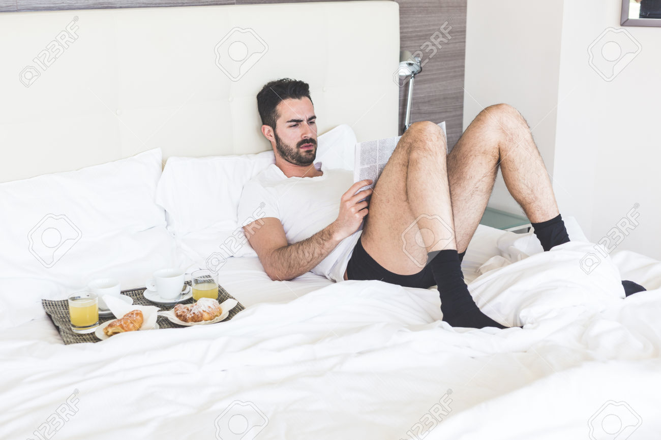 Man reading a newspaper lying on the bed